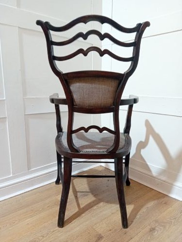 An antique dark mahogany Edwardian armchair featuring a contoured ladder back rest, padded central panel, curved armrests, and grey upholstered seat. View IX