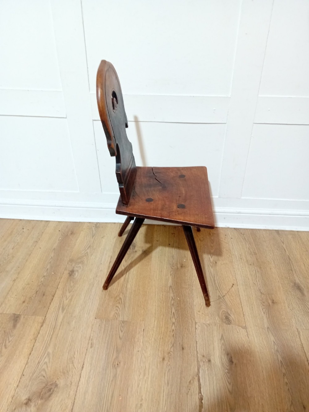 An antique Bavarian folk art wooden side chair featuring a carved cartouche backrest with a central cutout, a slab seat with visible joinery, and splayed legs. View VIII