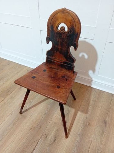 An antique Bavarian folk art wooden side chair featuring a carved cartouche backrest with a central cutout, a slab seat with visible joinery, and splayed legs.
