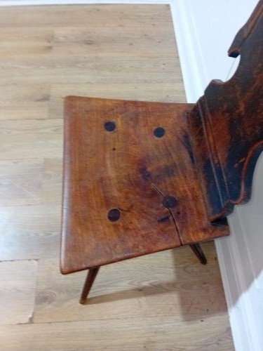 An antique Bavarian folk art wooden side chair featuring a carved cartouche backrest with a central cutout, a slab seat with visible joinery, and splayed legs. View V