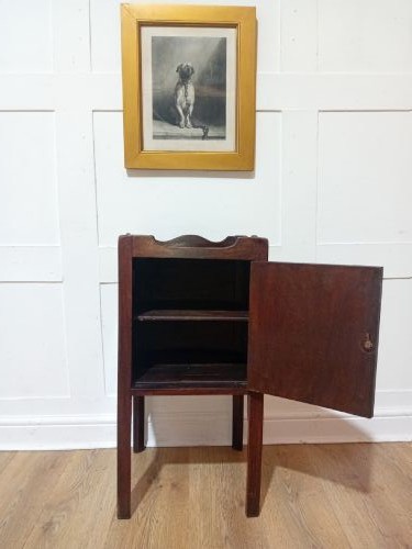 An 18th-century Georgian dark mahogany bedside cabinet featuring a galleried tray top with cut-out handles and a single panelled cupboard door resting on square legs. View V