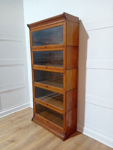 An Edwardian golden oak five-tier sectional barrister bookcase featuring glazed lifting doors with brass handles and a moulded top cornice. View II