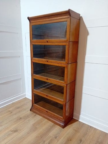 An Edwardian golden oak five-tier sectional barrister bookcase featuring glazed lifting doors with brass handles and a moulded top cornice. View VI