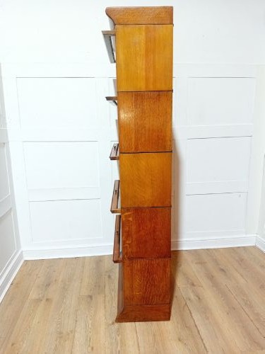 An Edwardian golden oak five-tier sectional barrister bookcase featuring glazed lifting doors with brass handles and a moulded top cornice. View XII