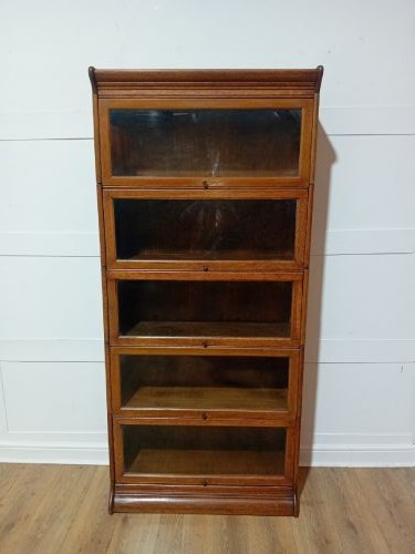 An Edwardian golden oak five-tier sectional barrister bookcase featuring glazed lifting doors with brass handles and a moulded top cornice. View XV