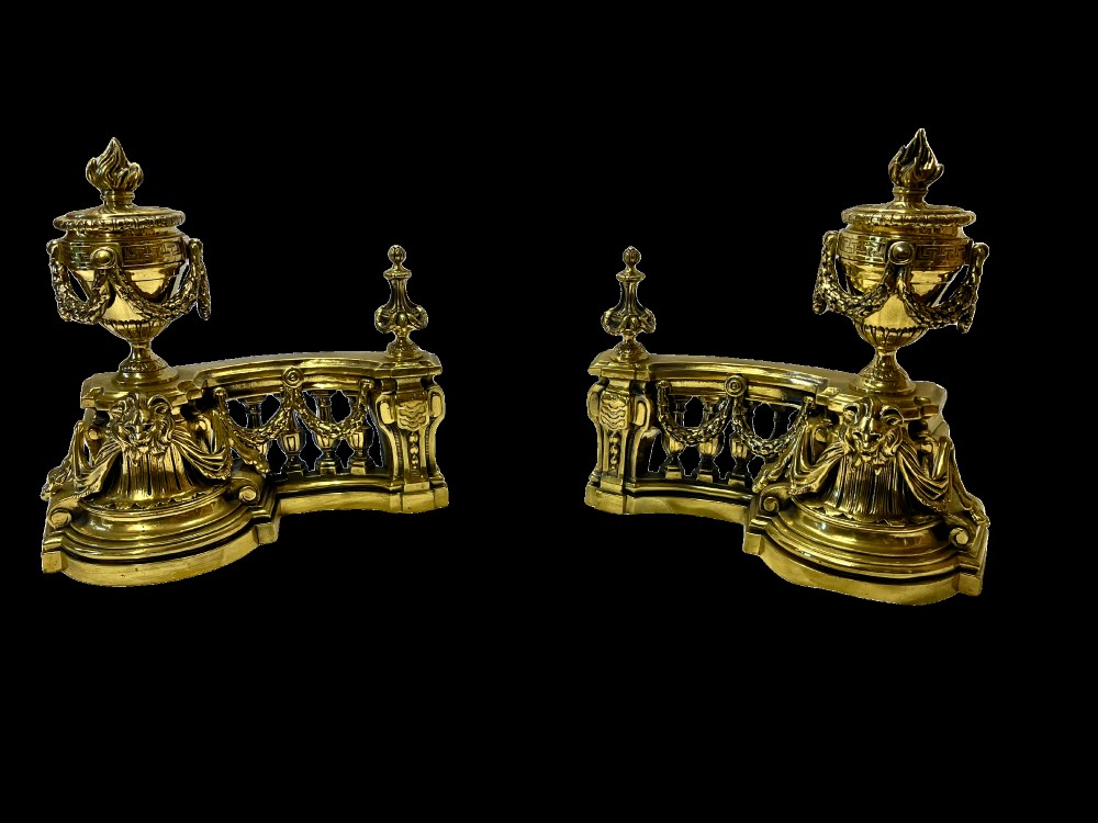 A pair of ornate brass fire dogs in the Louis XVI style, featuring draped flaming urns atop balustraded bases. View II