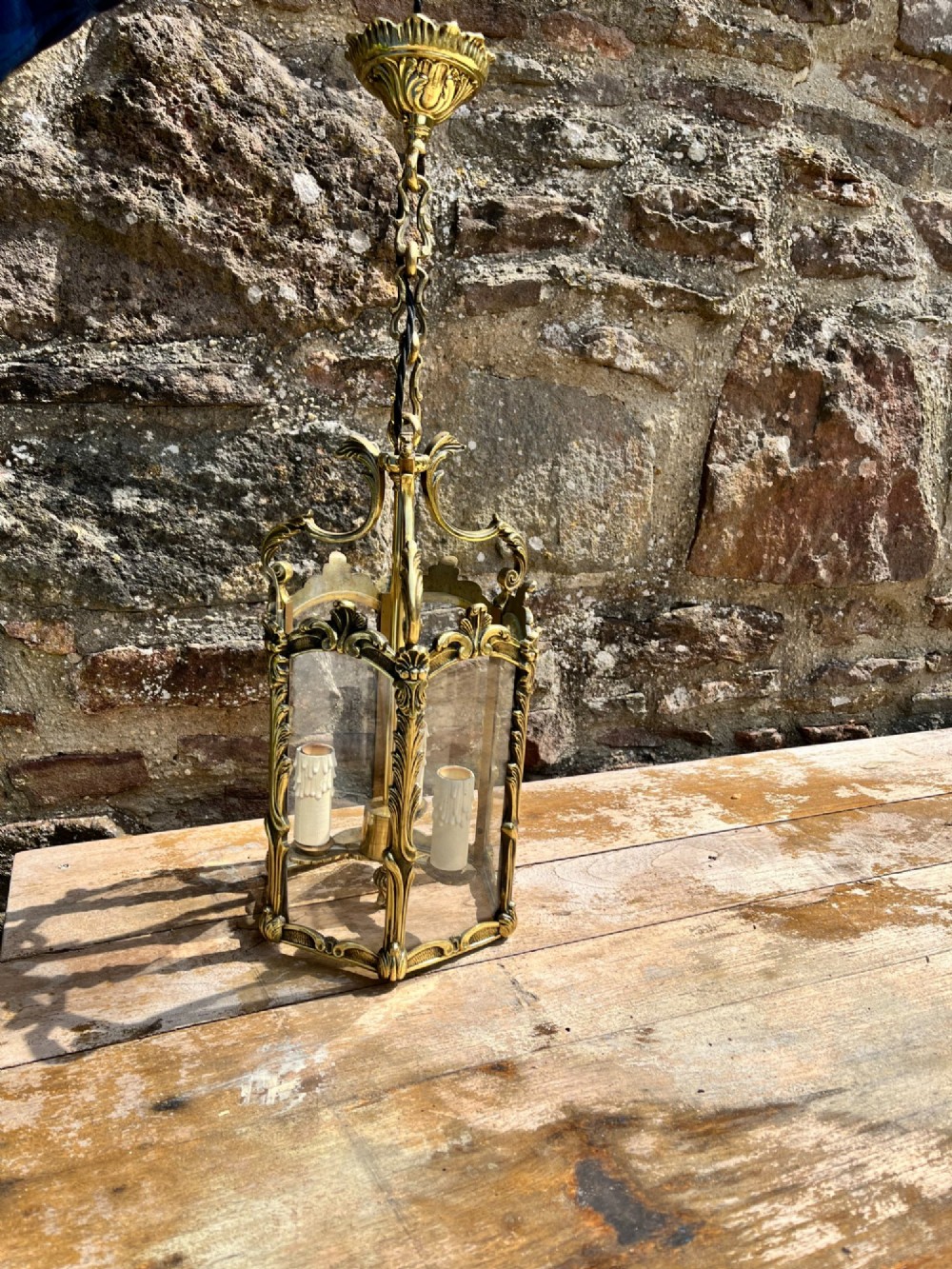 An ornate French style brass hanging hall lantern featuring glazed panels, acanthus scroll details, and three interior faux candle light sockets. View III