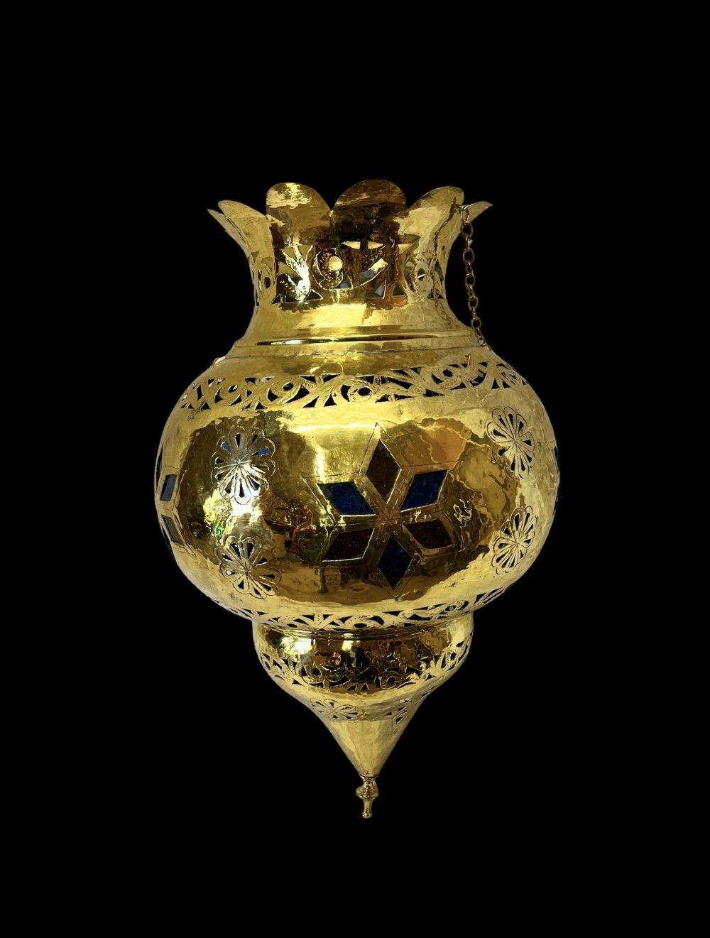 A pierced brass hanging lantern featuring floral and geometric fretwork, blue glass inserts, a flared scalloped rim, and a pointed base finial.