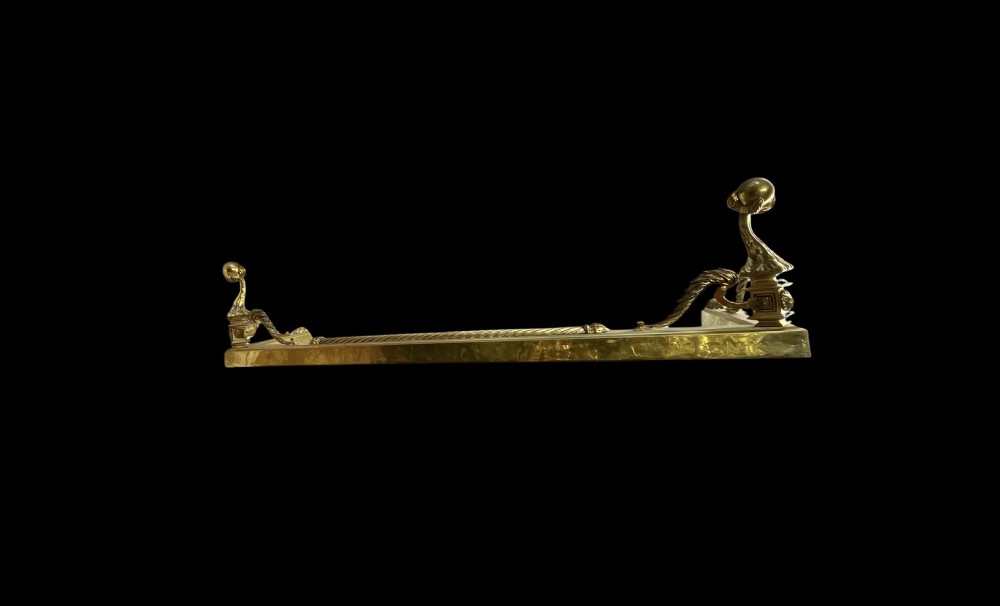 An Edwardian polished brass fireplace fender with decorative end finials and a low moulded base.