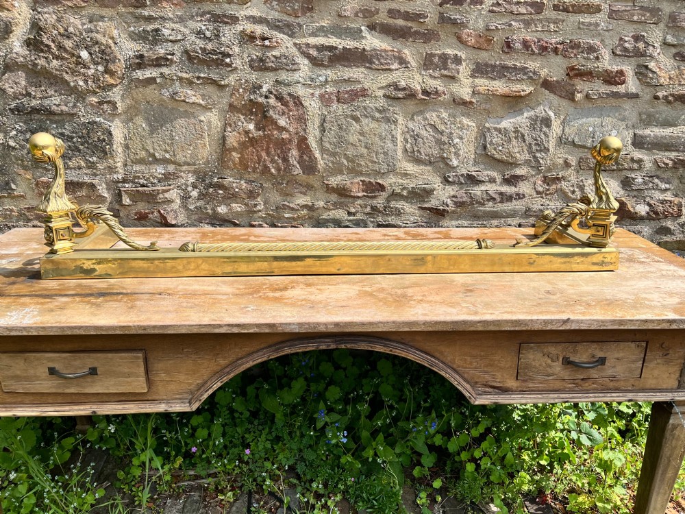 An Edwardian polished brass fireplace fender with decorative end finials and a low moulded base. View V