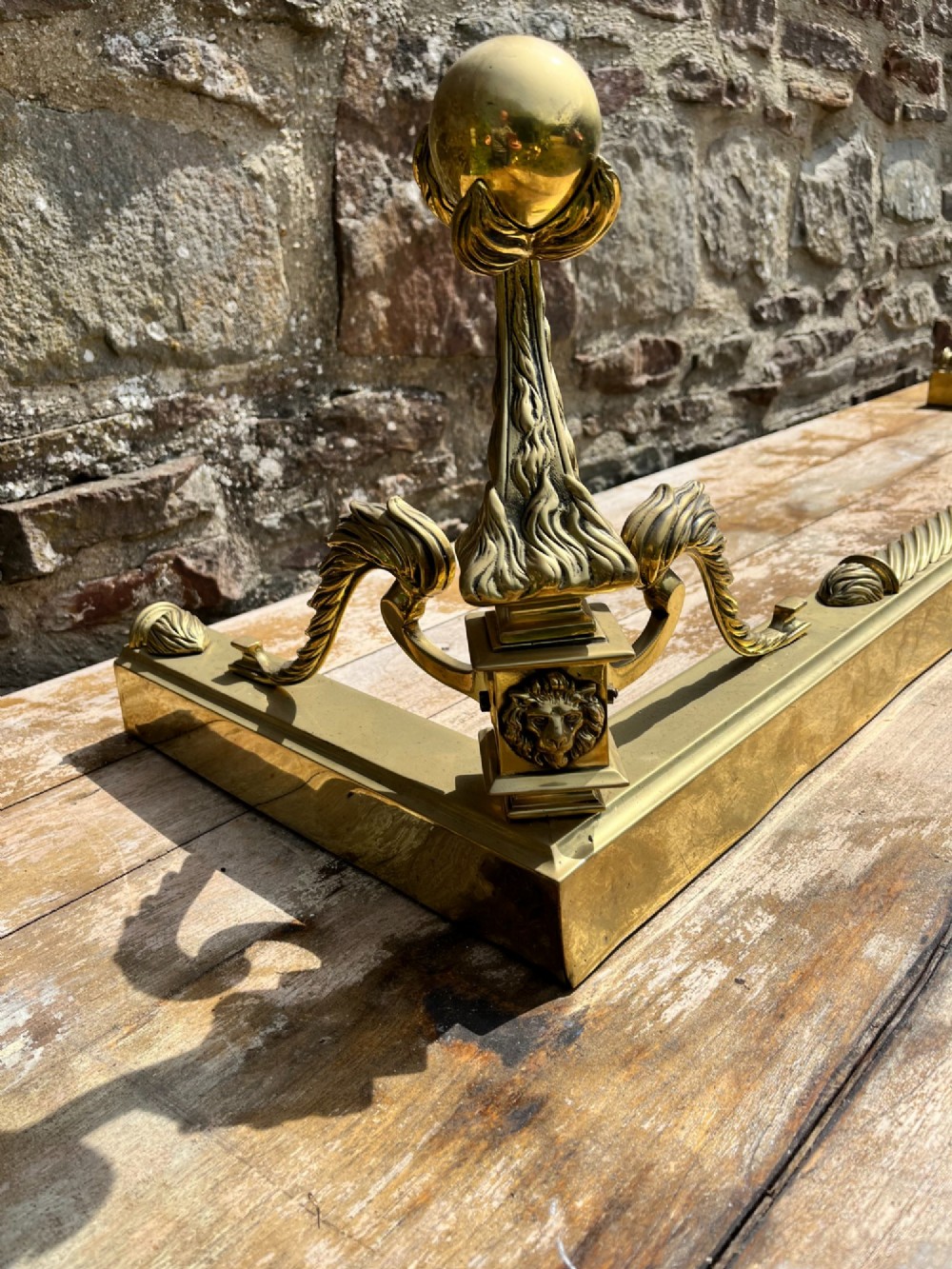 An Edwardian polished brass fireplace fender with decorative end finials and a low moulded base. View II