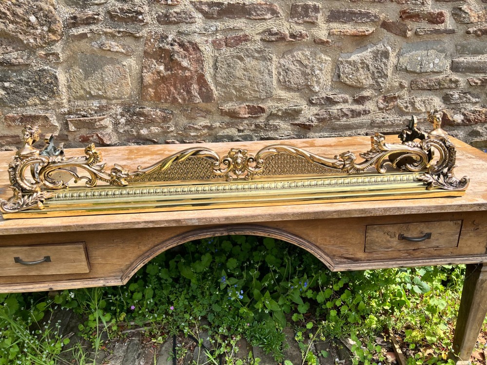 An ornate brass and bronze fireplace fender featuring Rococo scrollwork, lattice panels, and female figural end ornaments. View VII