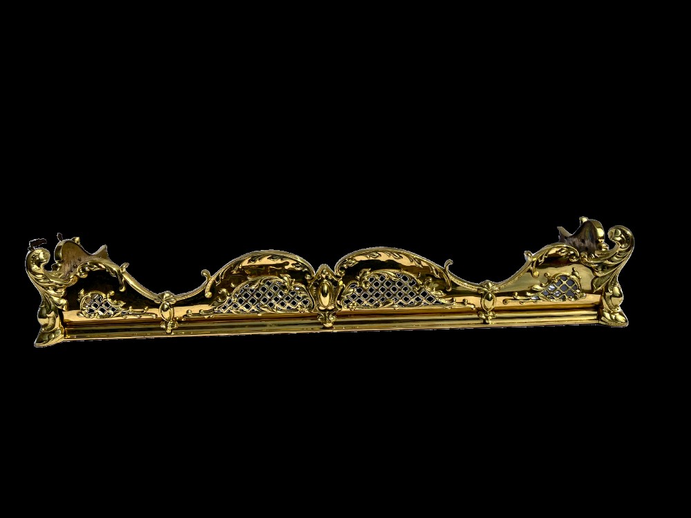 A late Victorian polished brass fireplace fender featuring pierced lattice panels, scrolling Rococo cresting, and shaped corner mounts against a dark background. View III