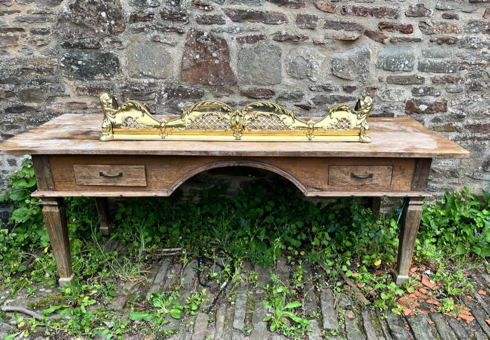 A late Victorian polished brass fireplace fender featuring pierced lattice panels, scrolling Rococo cresting, and shaped corner mounts against a dark background. View II