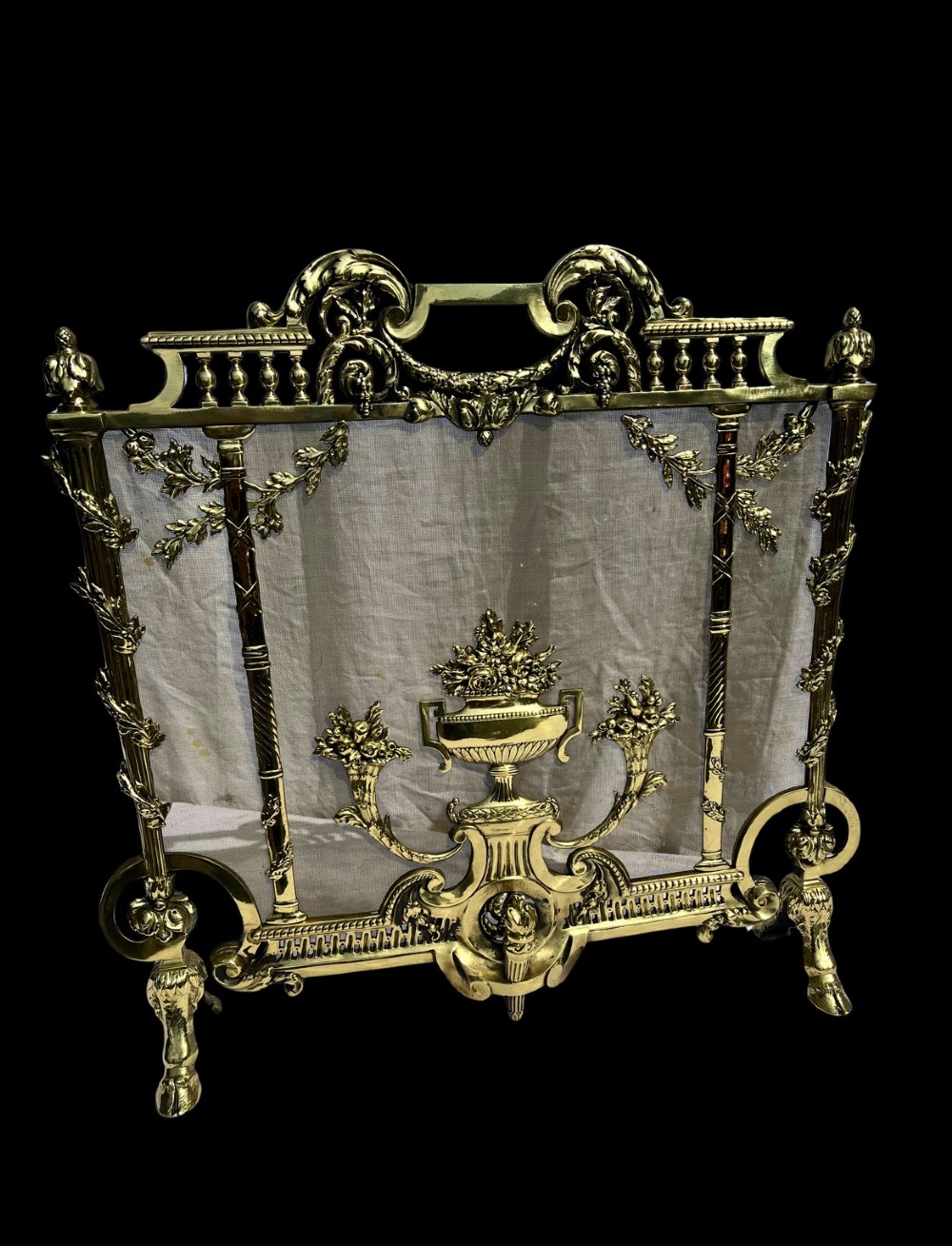 A cast brass fire screen featuring ornate scrollwork, a central urn motif, floral swags, and a mesh background panel.