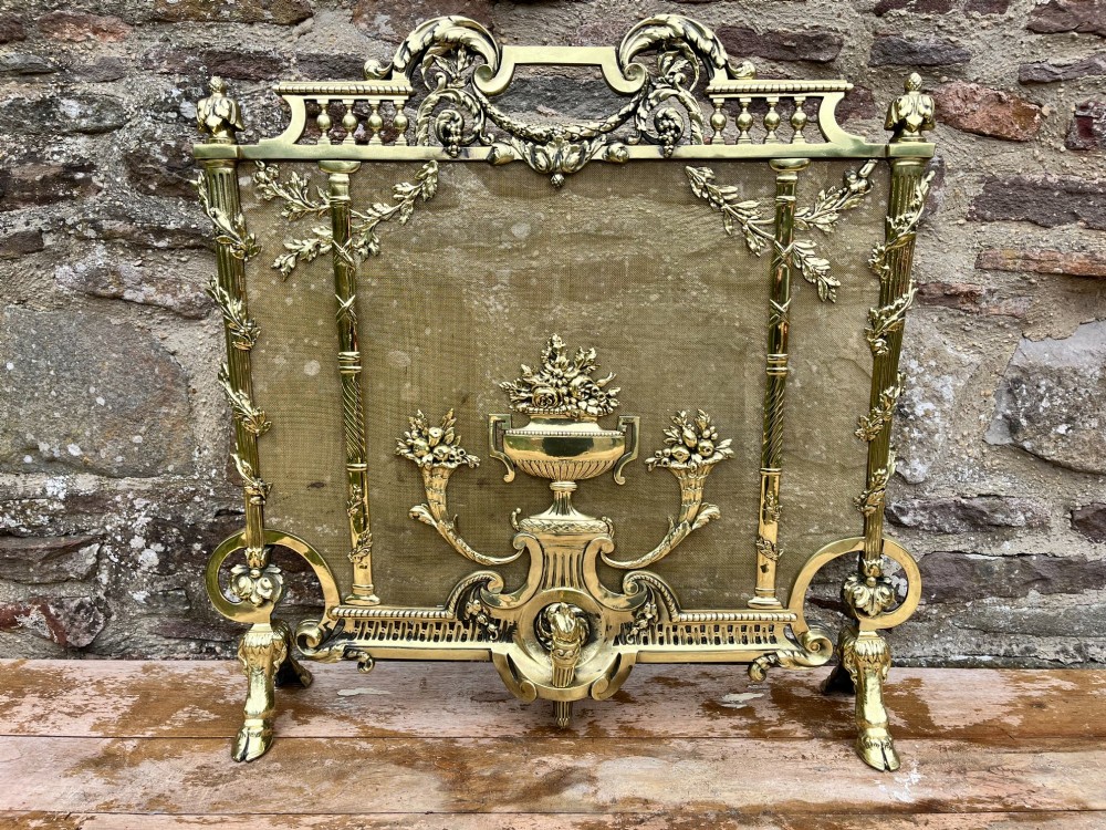 A cast brass fire screen featuring ornate scrollwork, a central urn motif, floral swags, and a mesh background panel. View III