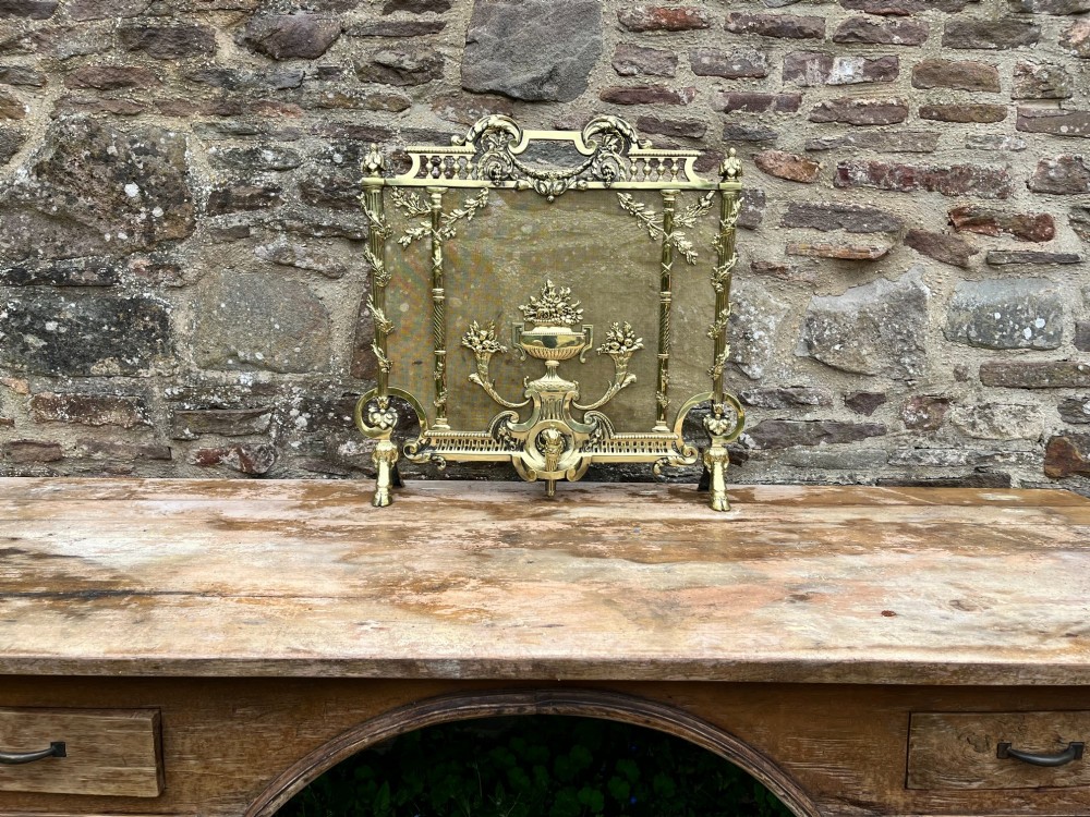 A cast brass fire screen featuring ornate scrollwork, a central urn motif, floral swags, and a mesh background panel. View IV