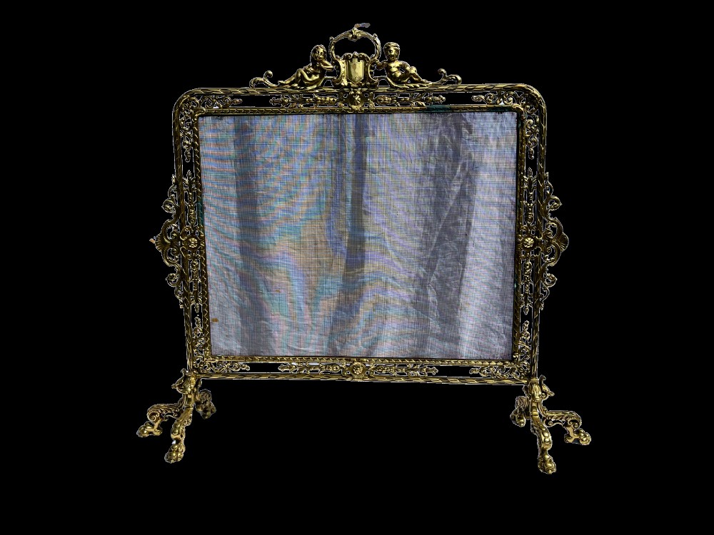 An ornate cast brass fire screen featuring cherub cresting, foliate side scrollwork, fine wire mesh insert, and four decorative feet. View II