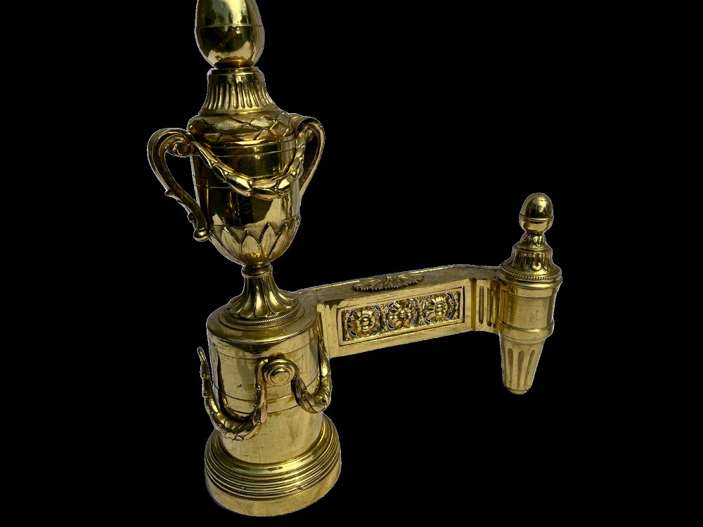 A pair of Neoclassical polished brass fire dogs featuring classical urn finials and garland swags. View III