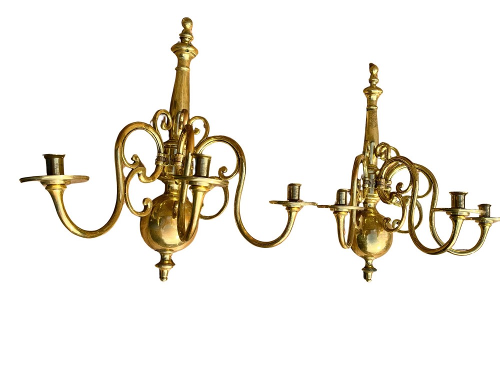 A pair of brass candle wall sconces featuring multi-branch scrolling arms, candle cups with drip pans, and turned central spindles.