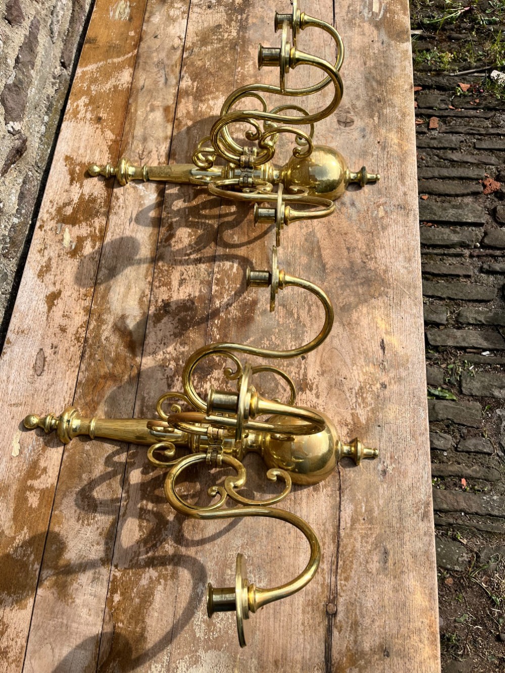 A pair of brass candle wall sconces featuring multi-branch scrolling arms, candle cups with drip pans, and turned central spindles. View IV