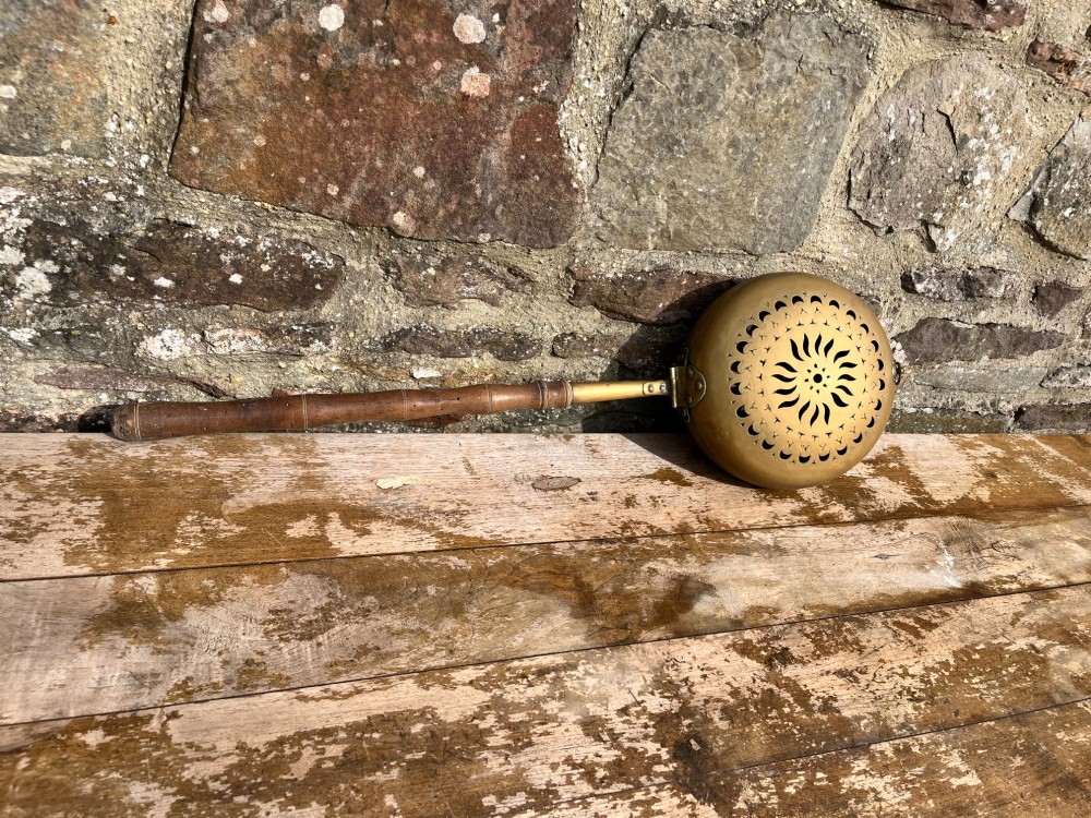 An antique English brass bed warming pan featuring a pierced decorative lid and a turned wooden handle. View V