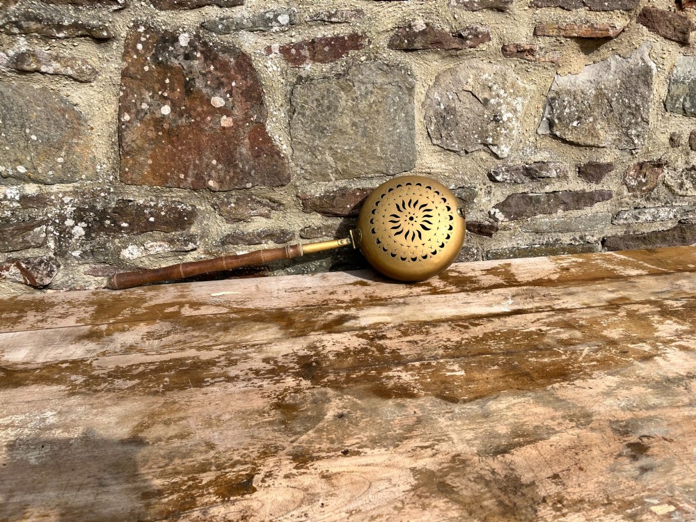An antique English brass bed warming pan featuring a pierced decorative lid and a turned wooden handle. View VI