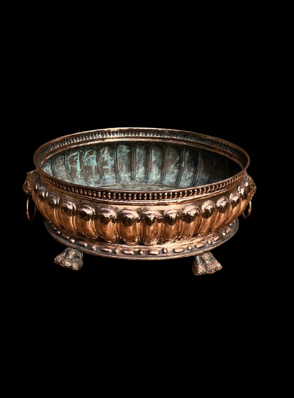 An antique circular copper jardiniere featuring gadrooned repousse patterns, side lion-mask ring handles, and three claw feet. View II