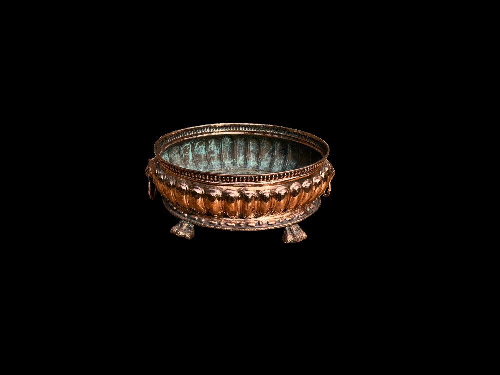 An antique circular copper jardiniere featuring gadrooned repousse patterns, side lion-mask ring handles, and three claw feet. View III