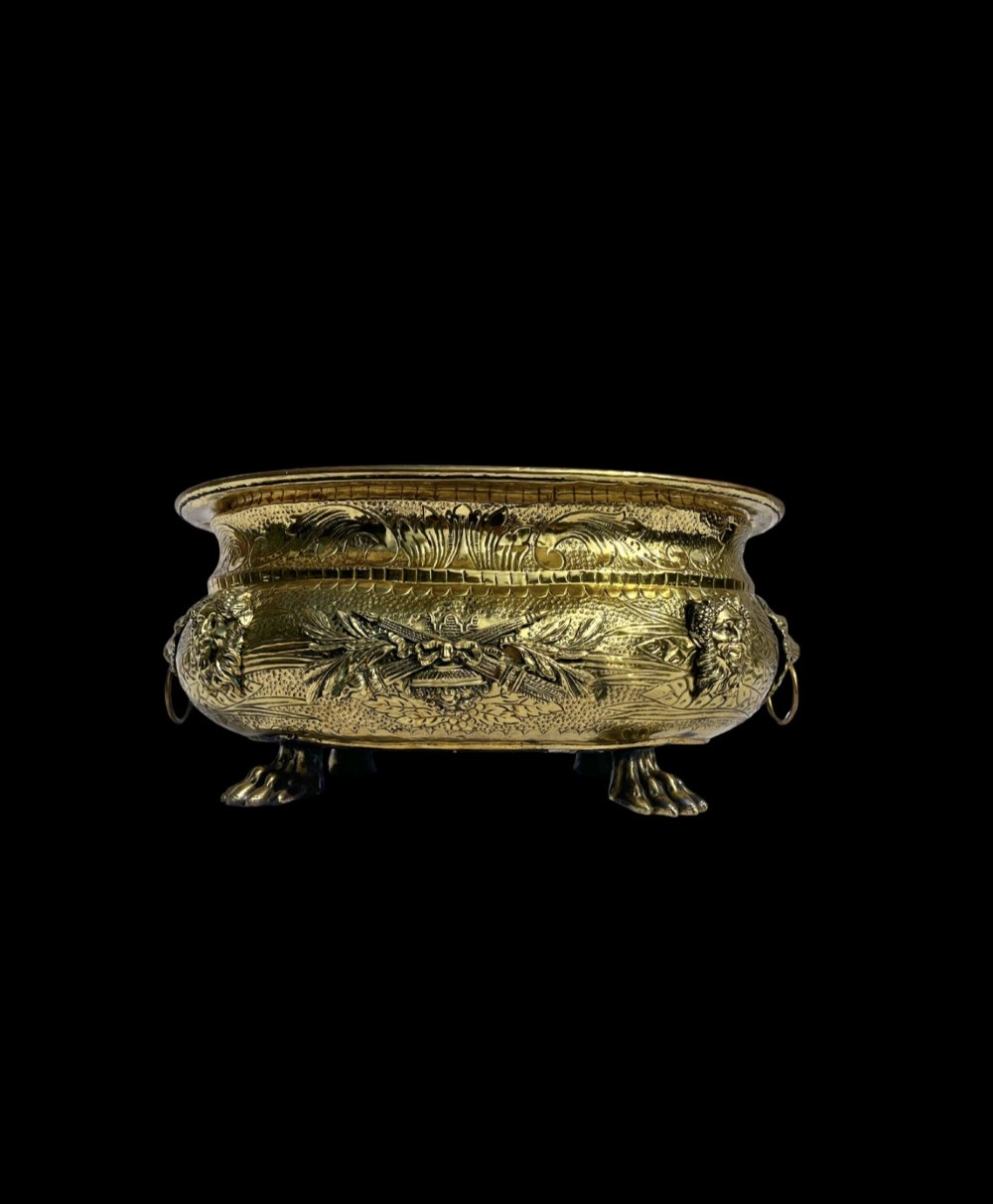 An embossed brass French jardiniere featuring side drop handles and lion mask details supported on claw feet.