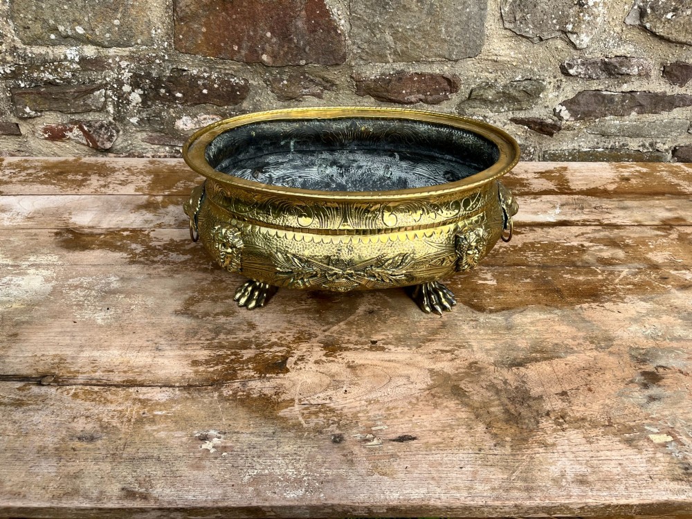 An embossed brass French jardiniere featuring side drop handles and lion mask details supported on claw feet. View V