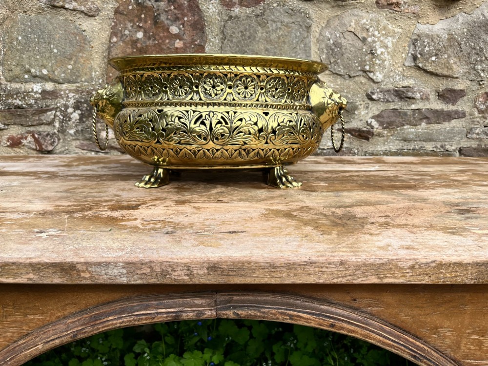 A round antique Dutch brass jardiniere featuring intricate repousse foliate patterning, dual lion-head ring handles, and claw feet. View III