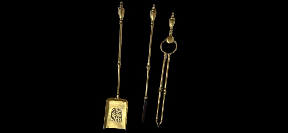 A three-piece set of polished brass fire tools featuring a pierced tray shovel, a poker, and tongs, all decorated with urn-shaped finials. View II