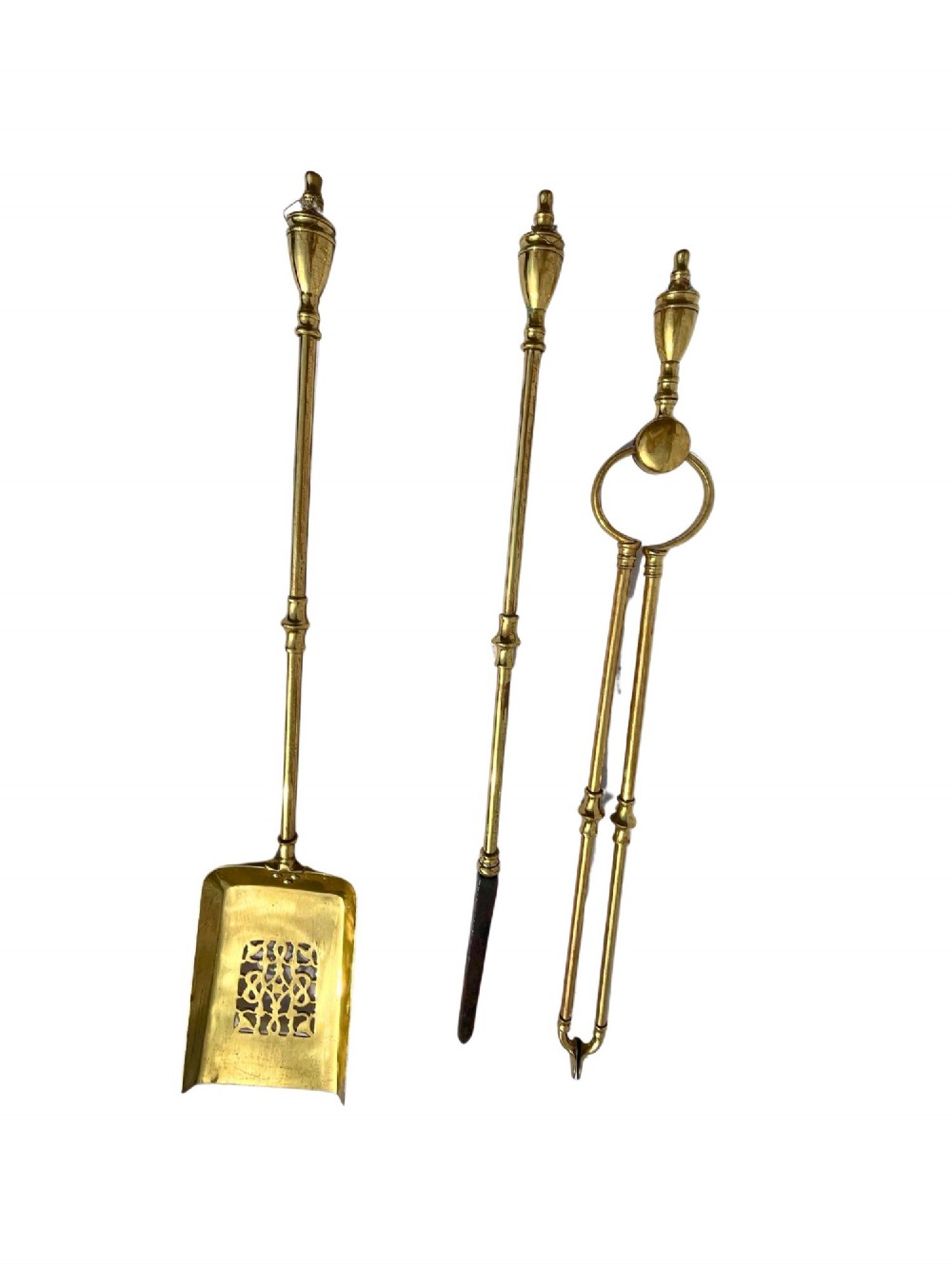 A three-piece set of polished brass fire tools featuring a pierced tray shovel, a poker, and tongs, all decorated with urn-shaped finials.