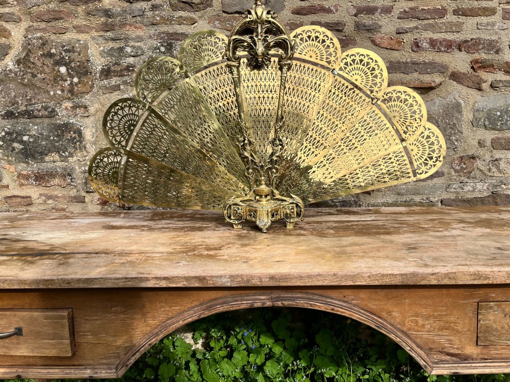 An antique folding brass fan fire screen featuring pierced filigree leaves and an ornate cast central handle. View VI