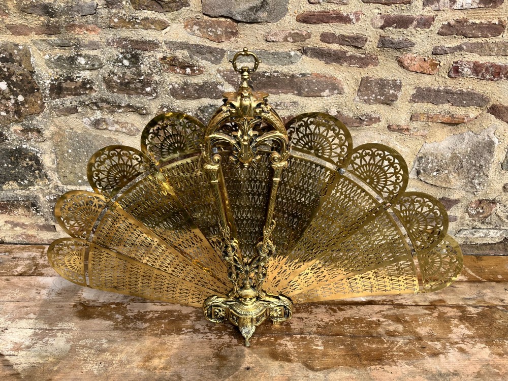 An antique folding brass fan fire screen featuring pierced filigree leaves and an ornate cast central handle. View II