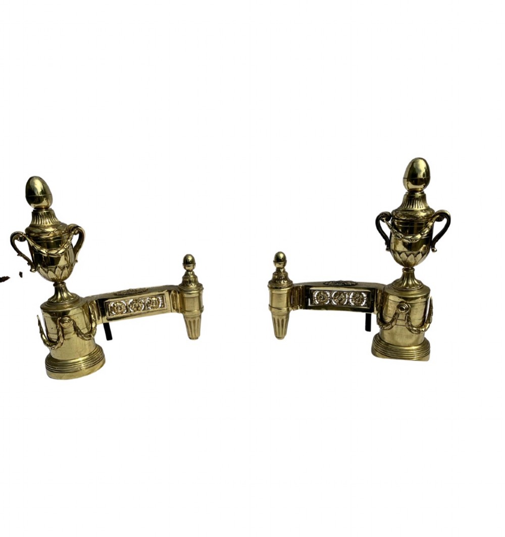 A pair of Neoclassical polished brass fire dogs featuring classical urn finials and garland swags.