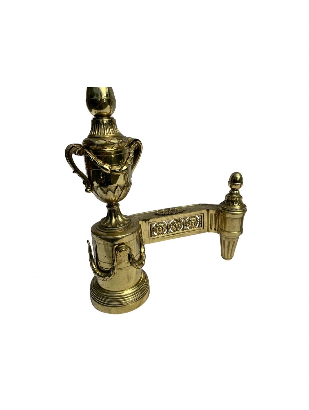 A pair of Neoclassical polished brass fire dogs featuring classical urn finials and garland swags. View IV