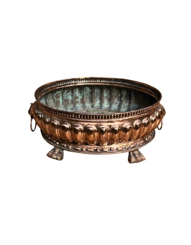 An antique circular copper jardiniere featuring gadrooned repousse patterns, side lion-mask ring handles, and three claw feet.
