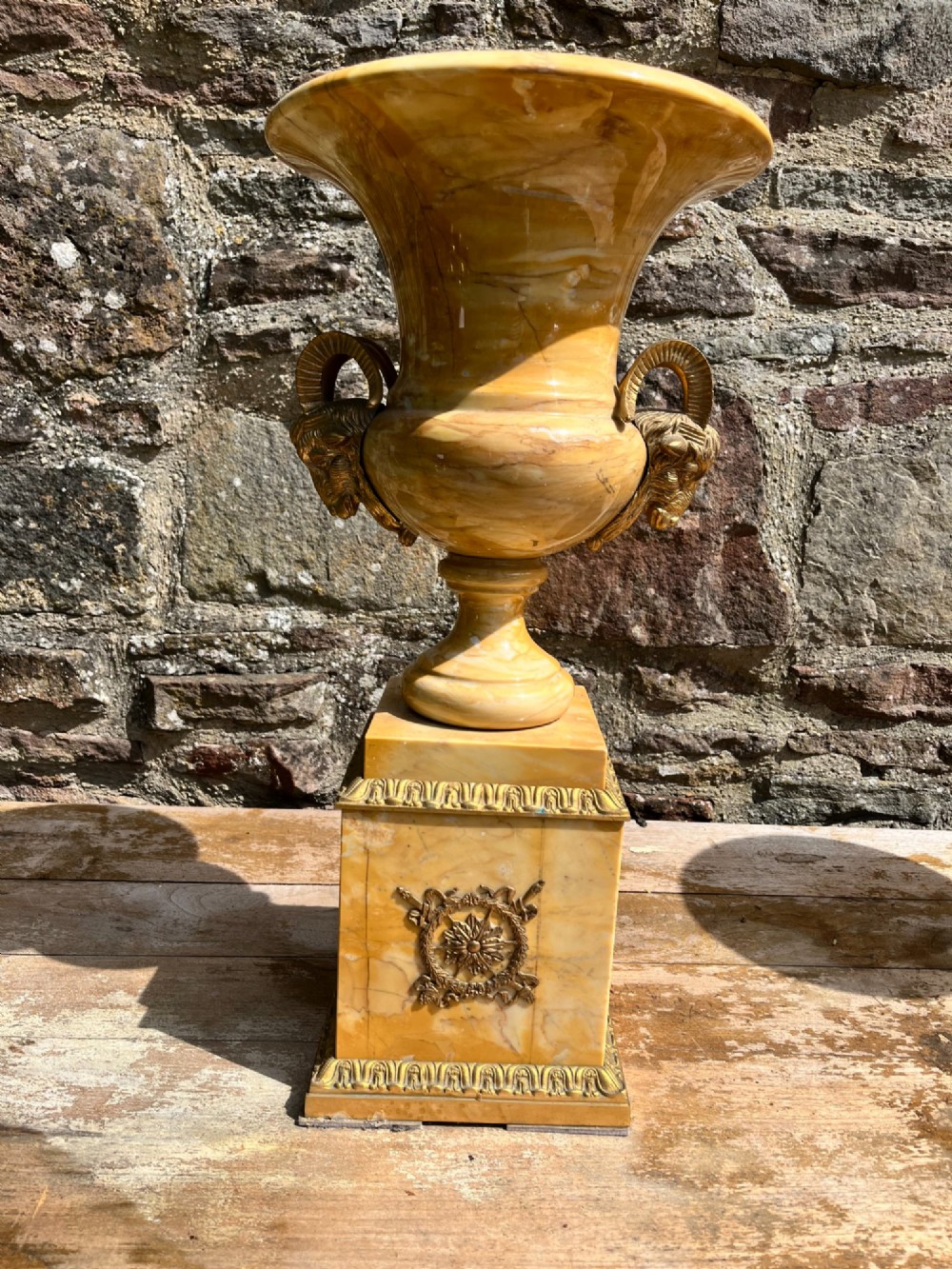 Pair of yellow veined Sienna marble campana urns featuring brass ram head handles and square plinths decorated with floral appliques. View V