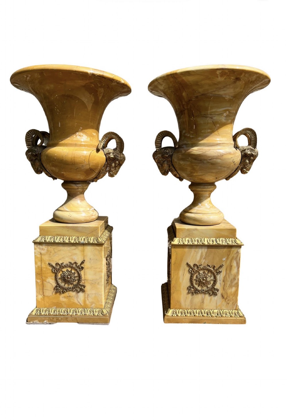 Pair of yellow veined Sienna marble campana urns featuring brass ram head handles and square plinths decorated with floral appliques.