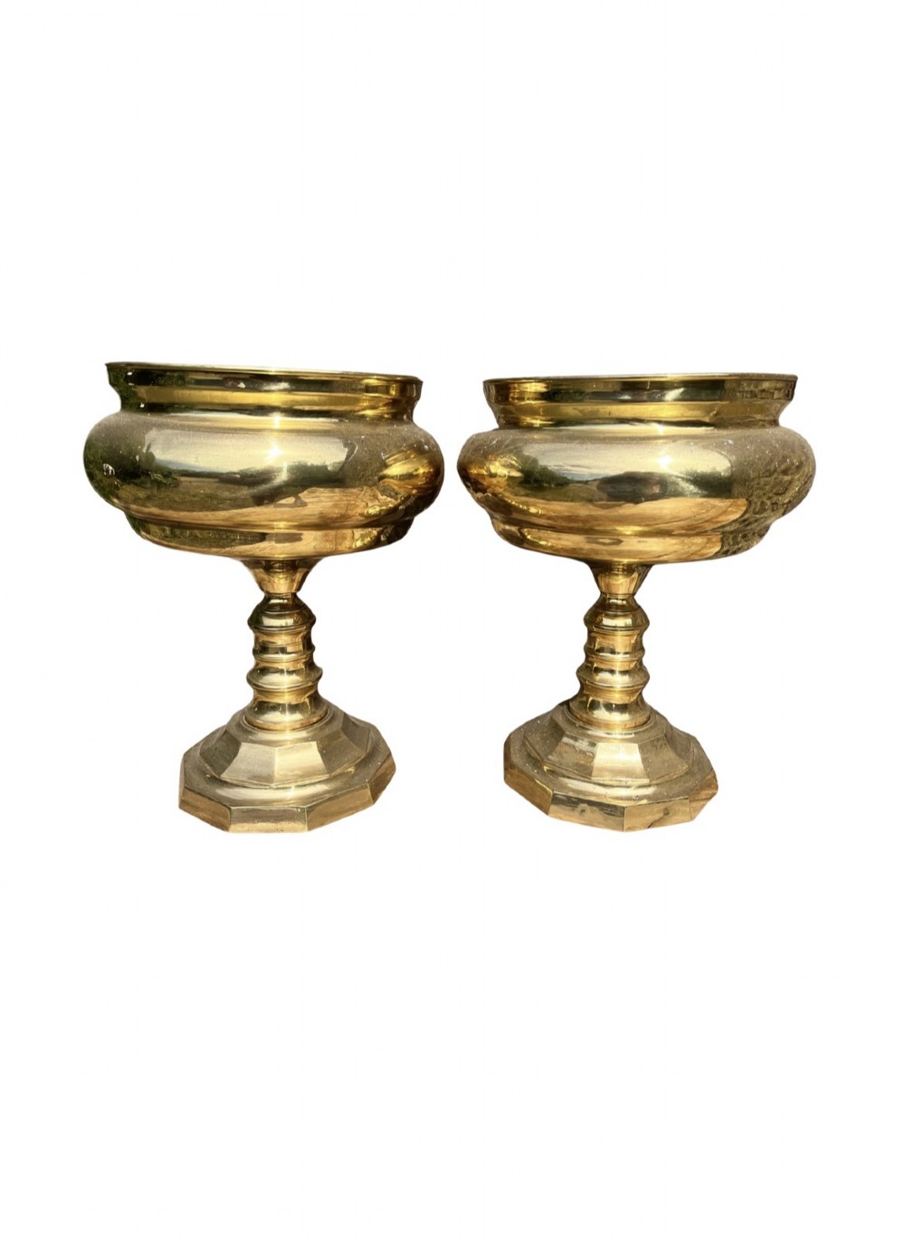 A pair of polished brass goblets featuring wide rounded bowls, turned baluster stems, and octagonal bases.