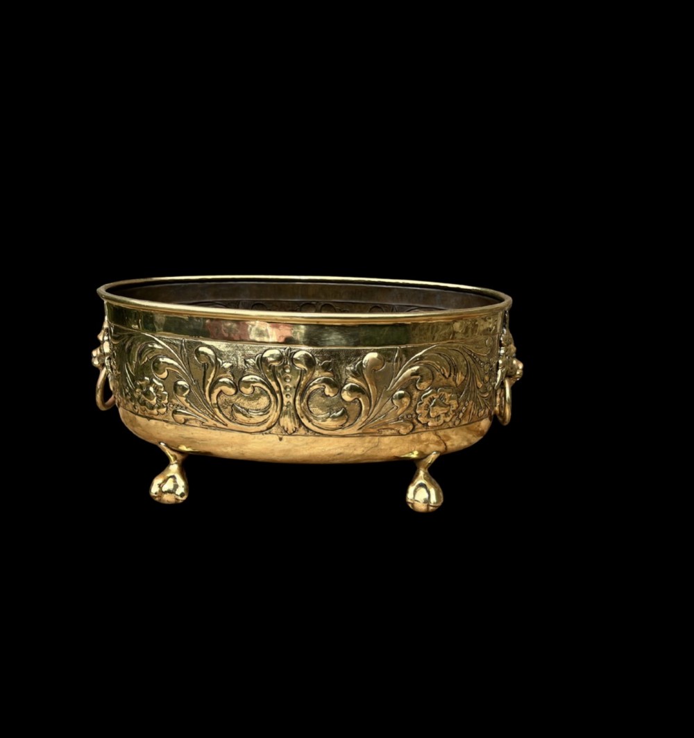 An oval brass jardiniere featuring embossed floral scrollwork, lion mask ring handles, and four claw feet. View III