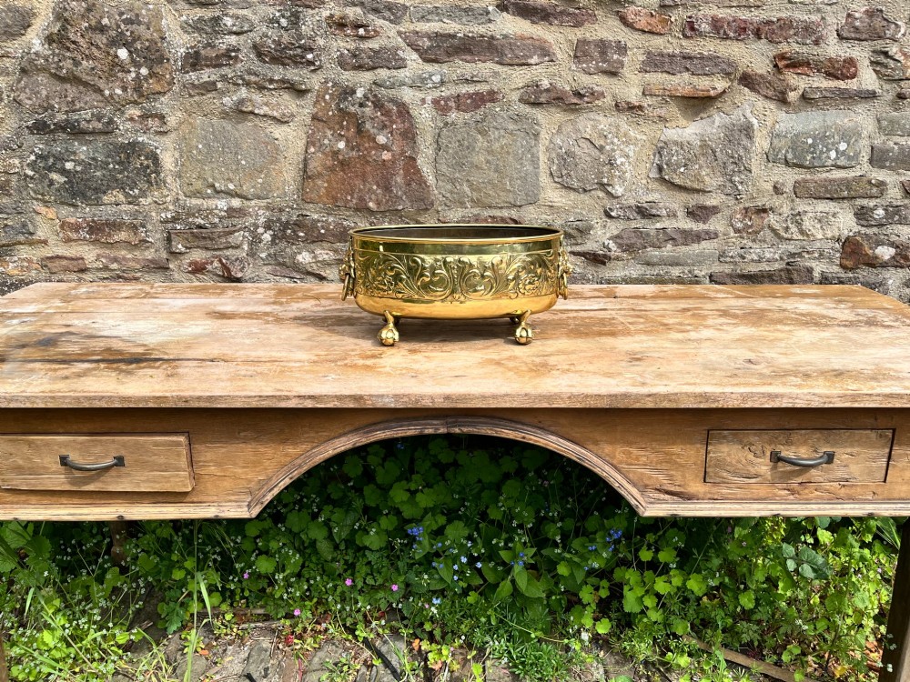 An oval brass jardiniere featuring embossed floral scrollwork, lion mask ring handles, and four claw feet. View VI