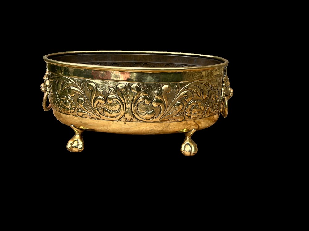 An oval brass jardiniere featuring embossed floral scrollwork, lion mask ring handles, and four claw feet. View II