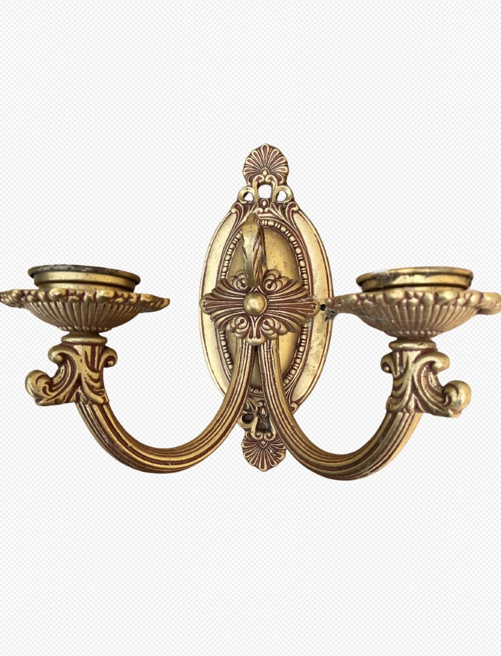 An ornate antique cast brass twin-arm wall sconce featuring an oval backplate decorated with classical motifs and two curved candle holders.