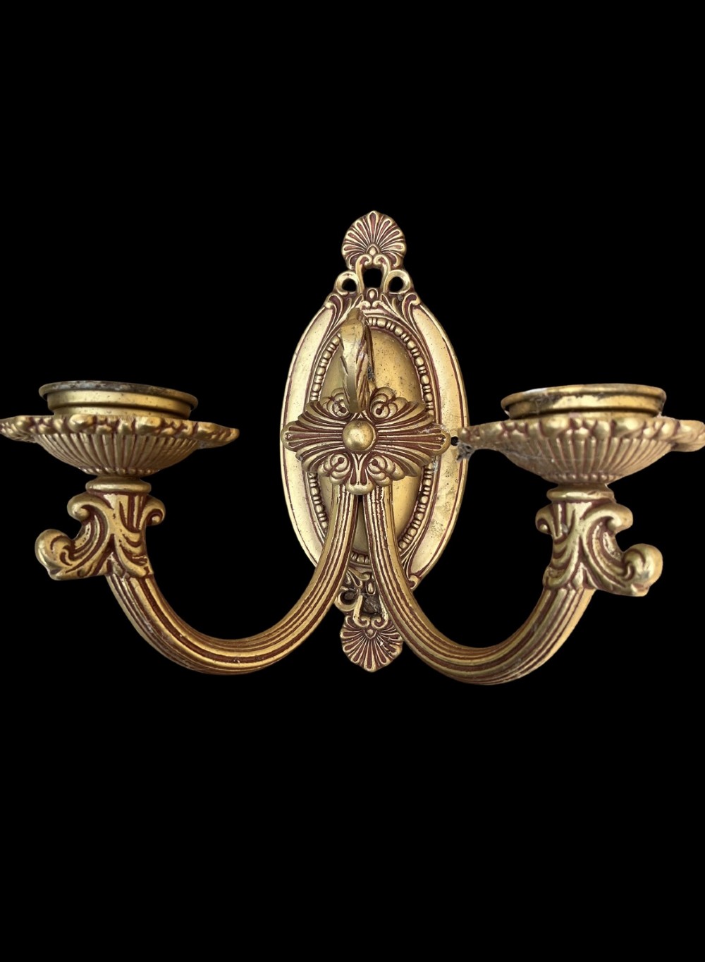 An ornate antique cast brass twin-arm wall sconce featuring an oval backplate decorated with classical motifs and two curved candle holders. View II