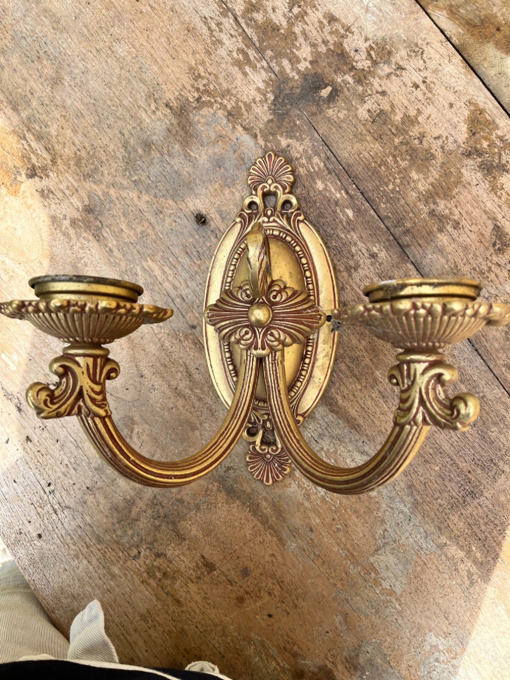 An ornate antique cast brass twin-arm wall sconce featuring an oval backplate decorated with classical motifs and two curved candle holders. View III