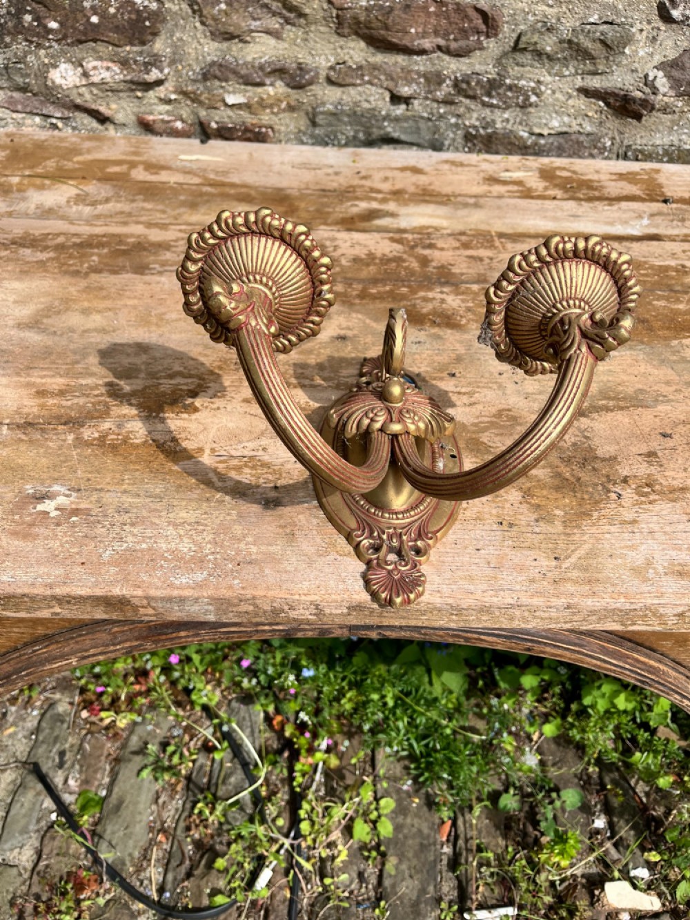 An ornate antique cast brass twin-arm wall sconce featuring an oval backplate decorated with classical motifs and two curved candle holders. View IV
