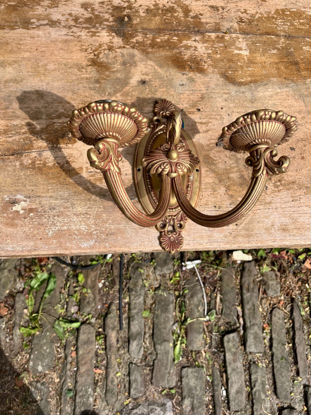 An ornate antique cast brass twin-arm wall sconce featuring an oval backplate decorated with classical motifs and two curved candle holders. View V